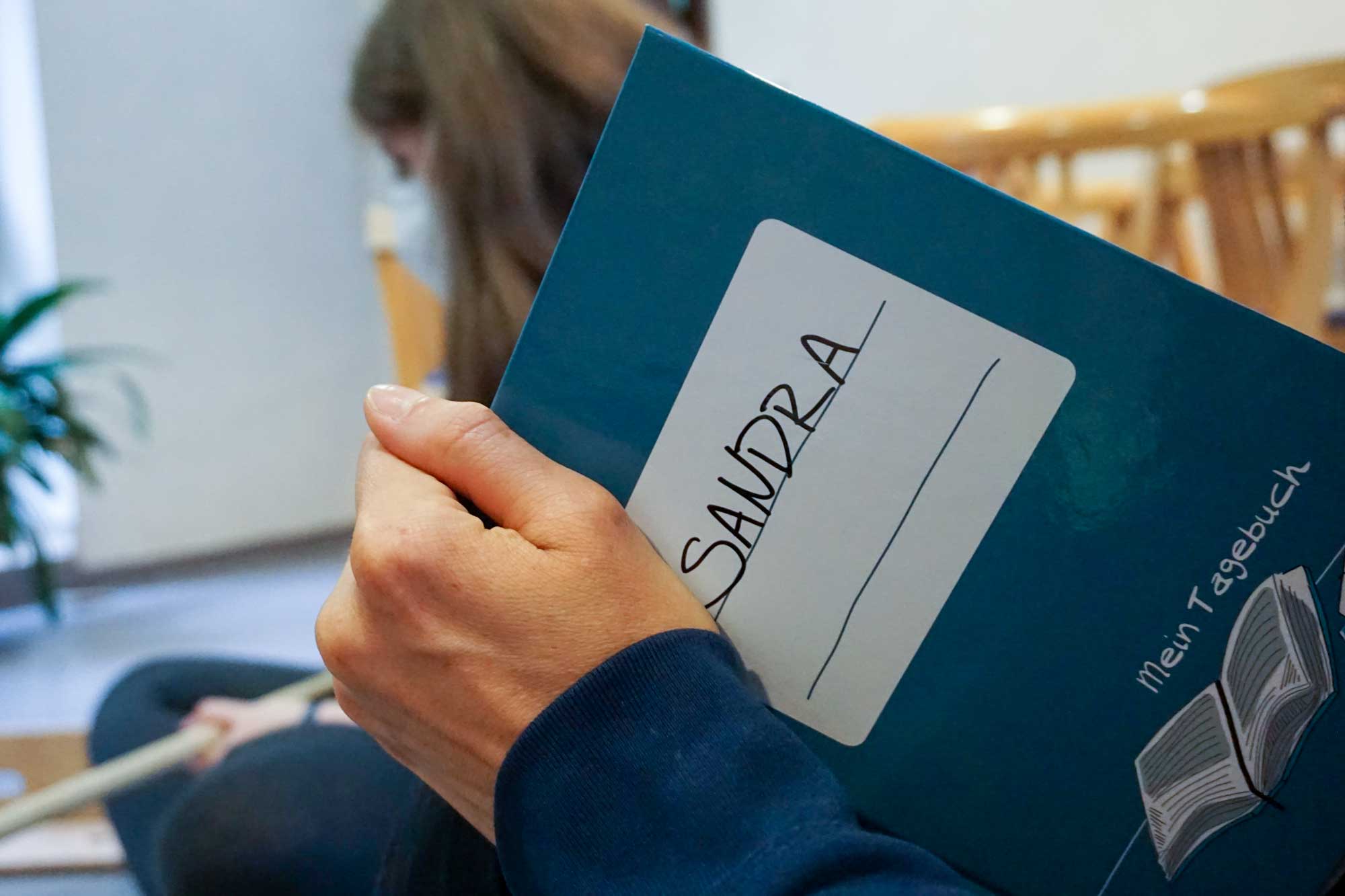 Eine Schülerin hält ihr Tagebuch, darauf steht "Sandra"
